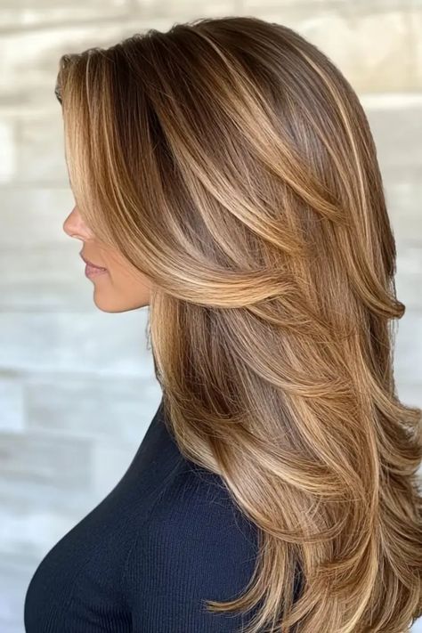 Woman with long, layered, light brown hair styled in soft waves, against a light gray background. Light Brown Hair Highlights And Lowlights, Fall Hair For Dirty Blonde, Honey Brown Hair Blonde Highlights, Caramel Hair With Blonde Highlights Golden Brown Low Lights, Carmel Hair Highlight, Honey Blonde Highlights On Light Brown Hair, Carmel And Blonde Highlights Brown Hair, Caramel Balayage On Light Brown Hair, Light Golden Brown Balayage