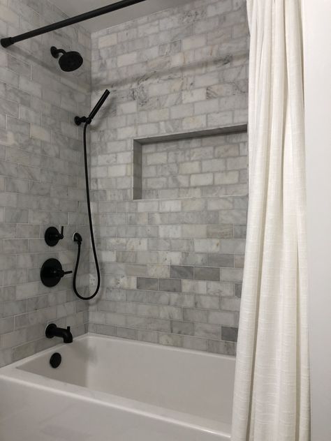 Farmhouse Shower Bathtub Combo - Matte Black Delta Fixtures with Floor and Decor Casa Antica Ocean Honed Marble Tile Redo Bathtub Shower Combo, Bathtub With Black Fixtures, Bathroom Remodel With Bathtub Shower Combo, Farmhouse Bathroom Bathtub Shower Combo, Extra Long Tub Shower Combo, Tub Shower Combo Remodel Farmhouse, White Tub Black Fixtures, Bathroom Ideas Bathtub Shower Combo, Tiling Around Bathtub Tub Surround