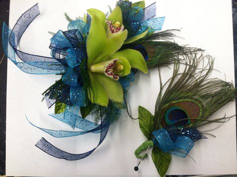 Peacock themed corsage and boutonniere (bout).  The corsage is made with green mini cymbidium orchids, a peacock feather, and double ribbon - blue cosmic ribbon and navy cosmic ribbon.  The boutonniere (bout) is made with a peacock feather, leaves, and a dual ribbon tuck to match the corsage.  By Tillie's Flower Shop  www.tilliesflowers.com Boutonniere And Corsage, Feather Boutonniere, Prom Corsage, Peacock Decor, Corsage And Boutonniere, Corsage Prom, Homecoming Dance, Prom Flowers, Cymbidium Orchids