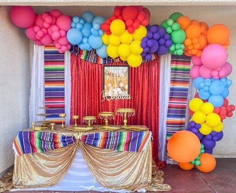 Create a fiesta-themed birthday party backdrop with vibrant décor accents. Drape white sequin curtains with red sequin curtains on a backdrop stand and decorate them with traditional striped runners to highlight the theme. Furthermore, install a colorful balloon garland to enhance the backdrop and exude liveliness all around. Dress up the dessert table using white & gold sequin tablecloths and place gold cake stands along with gold serving trays on top for a lavish display of delectable treats. Backdrop With Curtains, Gold Sequin Tablecloth, Event Decor Ideas, Party Decorations Table, Mexican Birthday Parties, Balloons Cake, Gold Cake Stand, Mexican Party Decorations, Birthday Party Backdrop