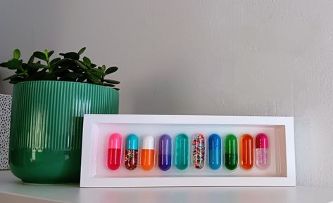 Colorful assortment of 10 chill pills in a white birch wood shadow box frame. Each pill (10) is hand-cast, pigmented, and hand painted in a fun variety of colors placed in a resin setting. This piece is sure to lighten up a home gallery wall or bring a pop of fun to a bookshelf in any office space. Variety and placement carefully selected to compliment each other and look great collectively. Pill Resin Art, Pill Art, Home Gallery Wall, Wall Bookshelf, Colorful Wall Hanging, Maximalist Wall, Maximalist Wall Art, Chill Pill, Wood Shadow Box