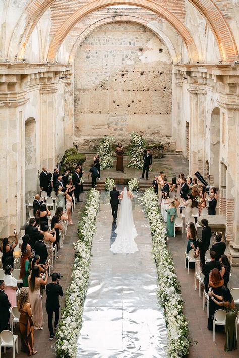 A bride with a long veil being escorted down the aisle lined with greenery and white flowers by her father toward the classic altar in a Guatemalan ruins ceremony space. Bride Walking Down Aisle, Guatemala Wedding, Spanish Style Wedding, Hacienda Wedding, Dominican Republic Wedding, Earthy Wedding, Spanish Wedding, Boda Mexicana, Santorini Wedding