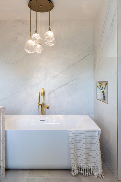 This modern bathroom has a freestanding white bathtub that's recessed into its own alcove. A sculptural multi-light pendant lamps with glass geometric shades, hangs above the bath, highlighting the design. #Bathtub #ModernBathroom Bathtub Lighting, White Bathtub, Bathroom Lighting Design, Brass Shower Head, Bathroom Lights, Bathroom Design Inspiration, Sparkling Lights, Wood Framed Mirror, Round Chandelier