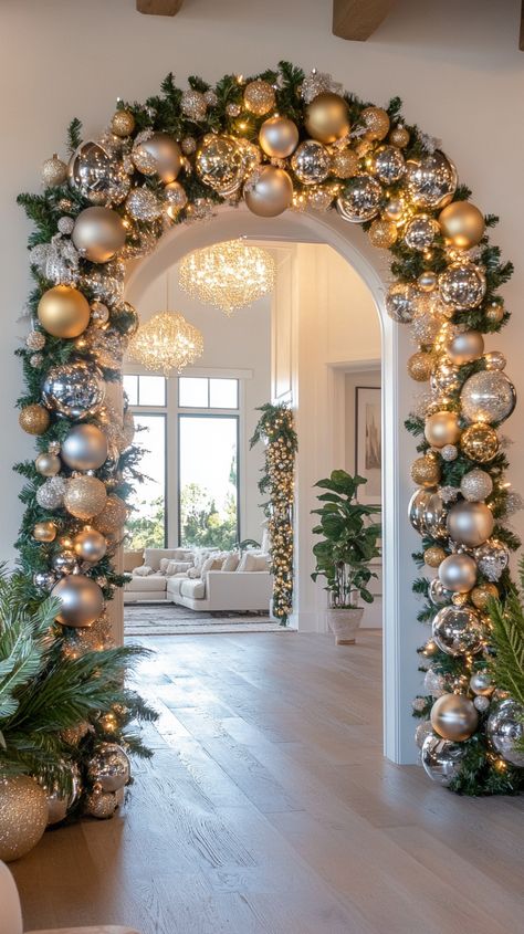 Festive living room with a gold and silver ornament garland over an archway, plush sofa, greenery, and warm lighting. Curio Cabinet Christmas Decor, Arched Doorway Christmas Decor, Indoor Column Christmas Decor, Archway Decor Living Room, Column Christmas Decor, Archway Christmas Decor Indoor, Archway Christmas Decor, Christmas Column Decor, Christmas Corner Decorations