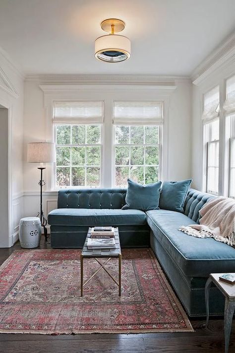 Transitional living room features a peacock blue velvet tufted sectional placed under windows dressed in white roman shades facing a slim black basket weave coffee table atop a red kilim rug. Blue Couch, Work Studio, Smart Tiles, Office Photo, Transitional Living, White Office, Banquette Seating, Work Spaces, Transitional Living Rooms