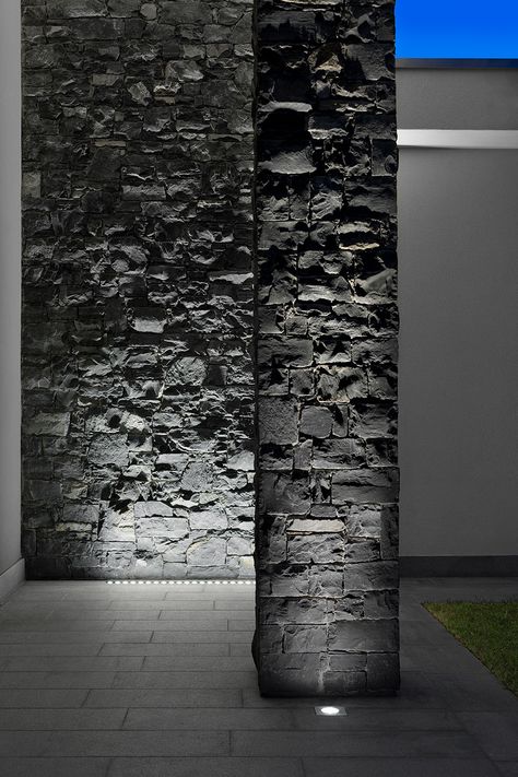 The exterior of the house is characterised by light-coloured surfaces combined with dark grey stone walls. The chosen lighting highlights the stone surface with a wall-grazing effect that underlines the surfaces’ materiality. Wall Grazing Lighting, Stone Wall Lighting, Stone Wall Light, Modern Exterior Lighting, Grey Stone Wall, Column Lighting, Stone Lighting, Stone Wall Design, تصميم داخلي فاخر