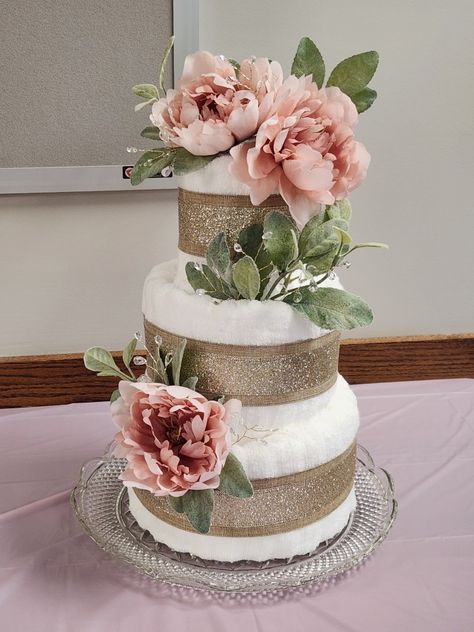 "Cake" layers are made of bath/hand towels and washcloths. Each layer is wrapped in a glitter burlap ribbon. Cake is decorated with fake lamb's ear, blush colored peonies, and a sprinkling of wired clear crystals. Wedding Cake Made Out Of Towels, Bridal Shower Towel Cake, Kitchen Towel Cakes, Wedding Towel Cakes, Shower Tower, Towel Cake, Towel Cakes, Lamb's Ear, Vintage Bridal Shower