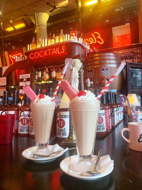 two chocolate milkshakes with pink wafers and red striped straws sitting at a 50s themed bar counter. red neon lights on the wall behind cast a red glow Date Chocolate, Date Shake, Diner Aesthetic, 1950s Diner, American Cafe, Milkshake Bar, 50s Diner, Vintage Diner, Retro Cafe