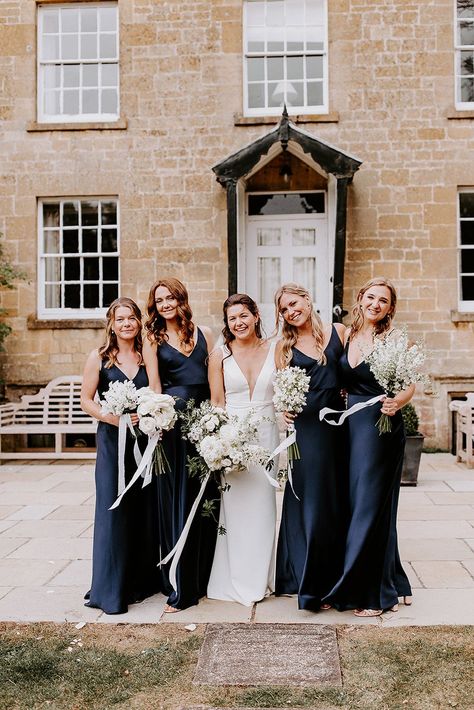 Bride in plunging Made With Love fitted wedding dress with bridesmaids in navy dresses holding white bouquets Navy Silk Bridesmaids Dresses, Satin Navy Blue Bridesmaid Dress, Dark Navy Bridesmaids, Navy Blue Flower Bouquet, Wedding Dress With Bridesmaids, Navy Blue Bridal Party, Navy Blue Wedding Party, Winter Wedding Bridal Party, Navy Bridal Party