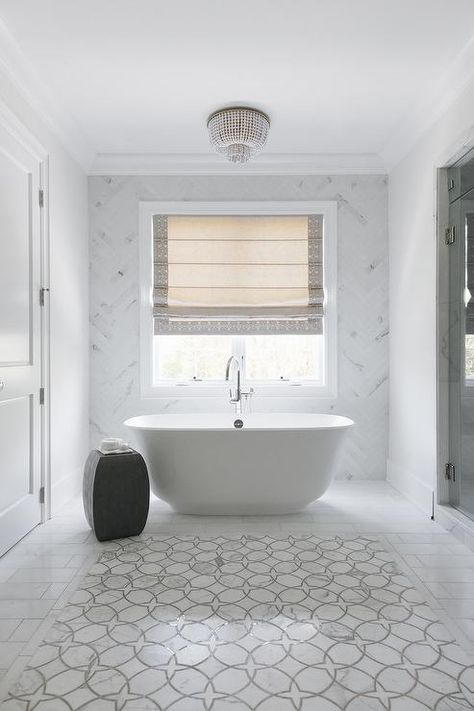 Framed by staggered marble tiles, white and gray marble accent tiles are mounted in front of an oval freestanding bathtub paired with a chrome floor mount tub filler and a black accent stool. Marble Herringbone Bathroom, Herringbone Bathroom, Bathroom Restoration, Marble Bathroom Floor, Marble Herringbone, Accent Tiles, Bathroom Accent Wall, White Marble Floor, Wallpaper Bathroom