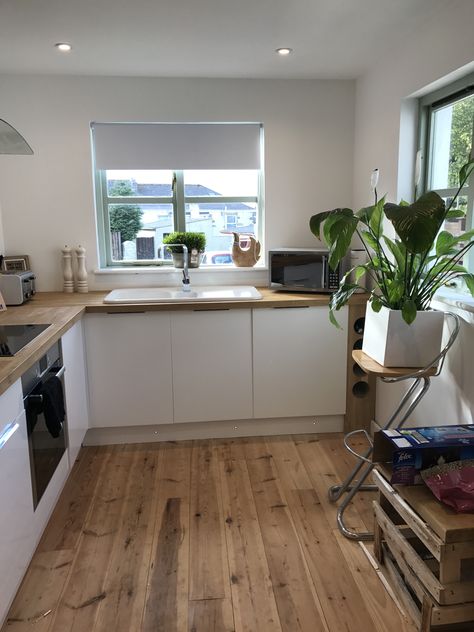 Natural kitchen theme. Ceramic white sink, oak tops, pine floorboards and gloss white doors with hidden flush handles.. and a Peace Lily to top it all off #kitchen #freshkitchen #neutralhome #floorboards #cottagekitchen #oakworktop #glosswhite White Kitchen Wooden Floor, Cream And Wood Kitchen, Slab Door Kitchen, Wooden Benchtop, Galley Kitchen Lighting, Matt White Kitchen, White Kitchen Handles, Pine Floorboards, Gloss Kitchen Cabinets