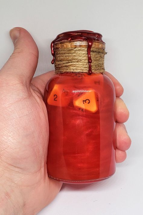 A large glass vial is held in hand. The glass is sealed with cork, twine, and red wax. Inside the glass bottle is a a swirling red liquid and several gaming dice. Dnd Dice Potion, Dnd Dice Roller, Dnd Health Potion, Potion Of Healing, Dnd Potions, Potion Maker, Potion Ideas, Inspo For Painting, Sensory Jars