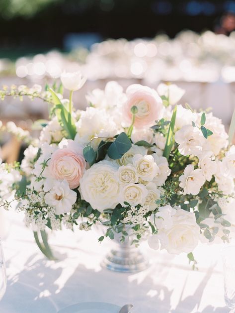 Rose Rock Floral gave this otherwise all-white centerpiece a little pop of color in the form of a few well-placed blush ranunculus. Assorted greenery gave the spread a "just picked" feel. Pink And White Flower Arrangements Wedding, Low Wedding Flower Centerpieces, Wedding Flower Centerpieces Elegant, Wedding Floral Needs, Wedding Florals White And Blush, Blush And White Centerpieces, Blush And White Wedding Flowers, Wedding Flowers White Centerpieces, Classic Wedding Florals