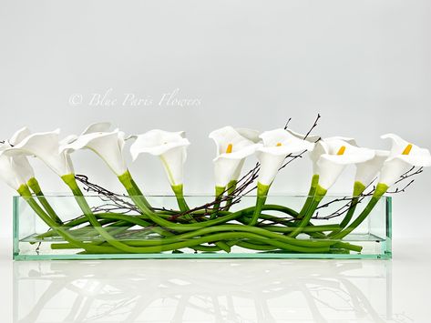 "Modern Long White REAL TOUCH Calla Lily Arrangement Artificial Faux Centerpiece Floral Flower Table Decor Silk Flowers Glass Vase French  * Arrangement comes in a 12\" or 24\" clear vase. (24\" arrangement shown on images)  * Feel free to contact us if you need more information about the arrangement. * At first look, people might not believe this is a permanent botanical design! * The arrangement contains the finest faux white calla lilies in a long rectangular glass vase. * The flowers have larger heads and they feel soft and lovely, real, and lively.  * All are arranged in a very modern and elegant long rectangular vase. * Perfect centerpiece on a long or rectangular dining table.  At Blue Paris Flowers we take pride in producing unique and luxurious floral designs. We handcraft each it Calla Lily Arrangement, Flowers Glass Vase, Flower Table Decor, Lily Arrangement, Calla Lily Centerpieces, Rectangle Vase, Orchid Flower Arrangements, Paris Flowers, Rectangular Vase