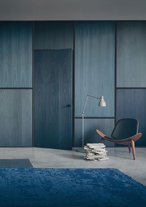 In this blue-hued space by Lissoni Associati Architecture, plywood-stained panels and doors in tone-on-tone muted shades of navy and indigo create the perfect backdrop for a minimalist mid-century display featuring the ever-popular Hans Wegner Shell Chair (interestingly also made out of plywood). Plywood House, درج السلم, Plywood Interior, Interior Design Minimalist, Plywood Walls, غرفة ملابس, Hidden Door, Design Room, Hus Inspiration