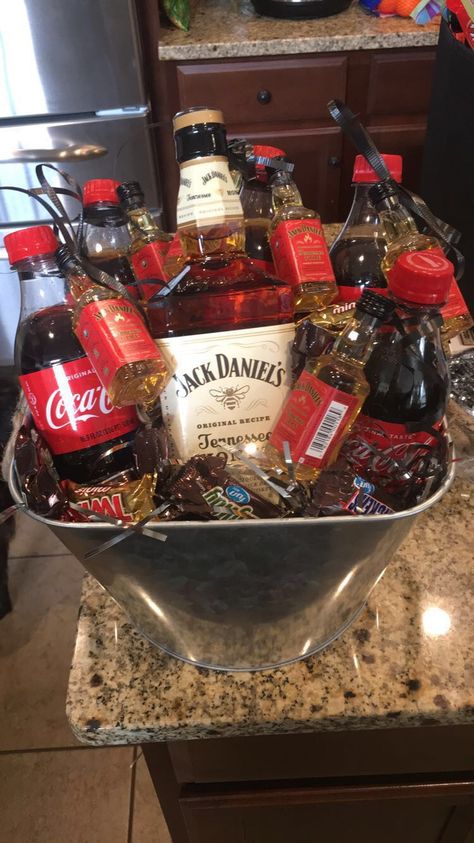 Adult liquor basket. Jack Daniels honey with Coke. Tied tiny airplane size bottles of Jack Daniels Fire around the necks w ribbon. Filled using air pockets from another shipment I received. Layer of tissue over that and then fav candy around bottles. Turned out cute and was a great adult birthday gift. Bucket can be used for ice or beer on ice around the pool. Valentines Gift Baskets, Alcohol Basket, Diy Christmas Gift Basket Ideas, Gift Basket Ideas For Women, Cheap Valentines Gifts, Alcohol Gift Baskets, Liquor Gift Baskets, Auction Gift Basket Ideas, Simple Valentines Gifts