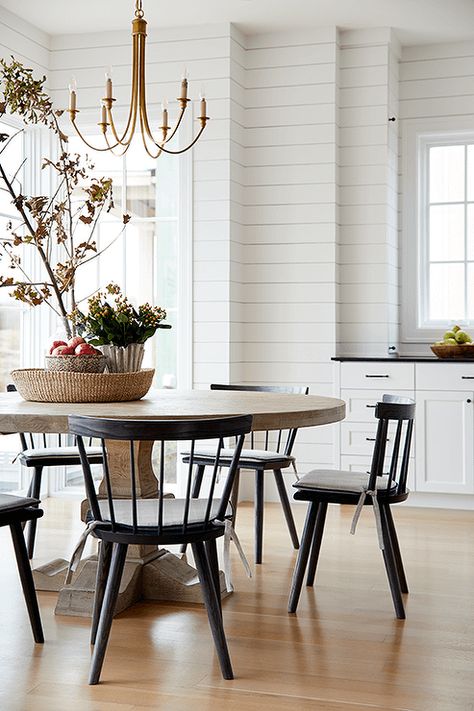 Black spindle chairs sit around a round brown dining table lit by a brass chandelier. Black Spindle Chairs, Spindle Chairs, Black Leather Dining Chairs, Spindle Chair, Brass Dining Table, Brown Dining Table, Black Chairs, Transitional Dining Room, Round Kitchen Table