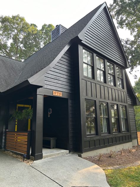 A-framed home with black exterior and black trim, two garage doors on side of house. Natural cedar accents Black House Exterior Paint, Sherwin Williams Caviar Exterior, Black Board And Batten Exterior, Black And Cedar House Exterior, Board And Batten Exterior, Three Story House, Black Houses, House Exterior Paint, Door Colors