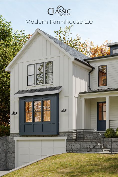 A modern farmhouse front exterior with drive under garage, white board and batten, grey stone, blue grey window assembly and front door. Board And Batten Bay Window Exterior, White Board And Batten Farmhouse, Board And Batten With Shakes Exterior, Light Grey Board And Batten Exterior, Gray Board And Batten Exterior, Grey Board And Batten Exterior, Board And Batton Exterior, White Board And Batten Exterior, Building Colour