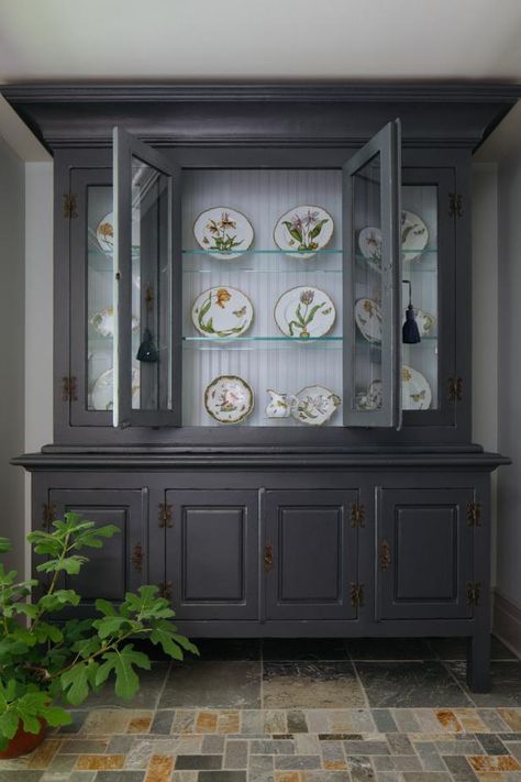 Tucked into a small nook, a large antique china cabinet features a dark exterior and a light interior. Glass shelves are tucked inside the cabinet and showcase decorative plates that add just the right amount of color and pattern to the neutral nook. A multicolor stone floor contrasts the white walls perfectly. Rustic Traditional Kitchen, Antique China Cabinet, Antique China Cabinets, Countryside Home, Redecorating Ideas, Stone Floor, Rustic Traditional, Cabinet Style, Countryside House