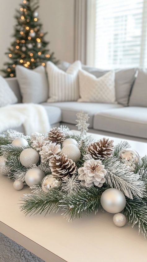 Elegant Christmas coffee table garland featuring white and silver decor, pine cones, and frosted evergreen branches in a cozy living room. Christmas Coffee Table, Table For Christmas, Silver Coffee Table, Christmas Coffee Table Decor, Table Garland, Festive Centerpieces, Christmas Decorations Living Room, Glass Balls, Elegant Centerpieces