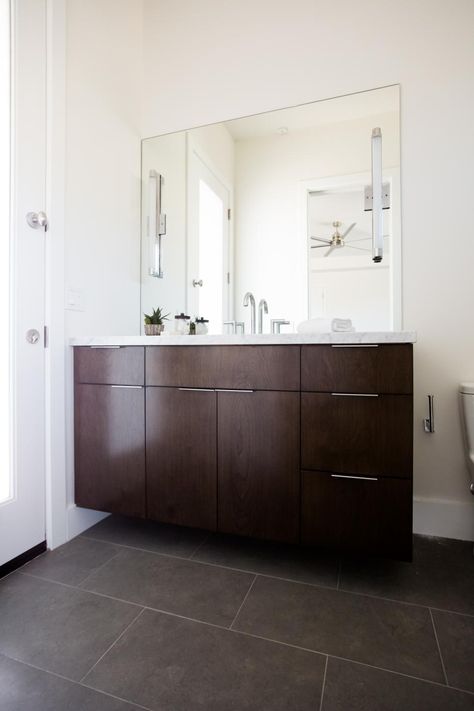 To add a touch of drama and depth to this otherwise white bathroom, Pure Design Interiors added a dark brown vanity and large brown floor tiles to complement the simple lines of the room. A large wall mirrors frames the entire vanity and slim, contemporary-styled cabinet pulls complete the look. Dark Brown Tile Floor, Dark Brown Bathroom Tiles, Dark Brown Bathroom Floor, Bathroom Dark Brown Floor, Brown Floor Tiles, Bathroom Brown Floor, Brown Floor Bathroom, Dark Brown Bathroom Vanity, Brown Tile Floor Bathroom