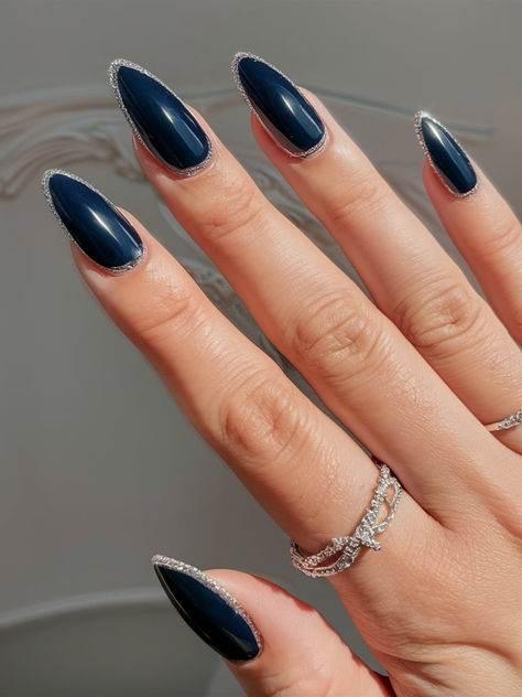 Dark blue nails with a glittering silver outline create a chic, refined look perfect for winter nights. The subtle sparkle along the edges enhances the depth of the color, adding elegance and sophistication to your January style. Dark Blue Nails With Silver Glitter, Navy Nails Design Winter, Navy And Silver French Tip Nails, Dark Blue And Glitter Nails, Silver And Dark Blue Nails, Dark Blue Nails Glitter, Dark Blue Nails With Silver, Glitter Outline Nails, Blue Elegant Nails