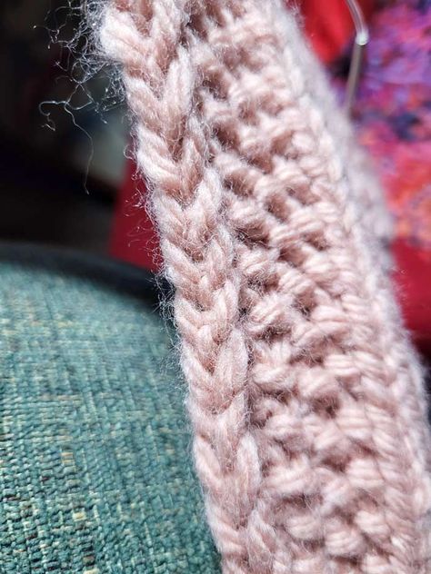 A close-up of the edge of a piece of peach-colored knitting showing a very neat chain edge going up the side of the seed stitch border, with one stitch of the stockinette stitch body of the scarf showing. The background is green on the lower left and red on the remainder; Lion Brand Hue + Me Seed Stitch Scarf, Learn To Knit, Pocket Scarves, Knit Edge, Seed Stitch, Moss Stitch, Lion Brand Yarn, How To Knit, Edge Stitch