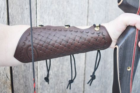 An arm guard to protect an archer's forearm from string slap. This one is extra long, with pointed ends and basketweave tooling. For archer's who want protection higher on their arm than the regular length arm guard will provide. It wraps around the forearm and is held in place by 3 stretch cord loops. Sized for wrist circumference of 5-10 inches.  Large end will fit forearm with a circumference of 8-15 inches. Left and right refers to the arm you intend to wear it on. Armguard is 8.5 inches long. Available in 3 colours. Arm Guard Archery, Leather Arm Guard, Archery Arm Guard, Forearm Guard, Arm Guards, Traditional Archery, Arm Guard, Archery, Left And Right