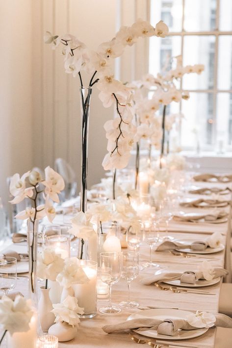 Elegant Luxury Wedding Reception Decor & Table Setup | Immerse yourself in the sophistication of this stunning rooftop wedding at 620 Loft & Garden in Manhattan! This chic wedding reception set up features delicate white orchids in tall, sleek vases, perfectly complemented by soft candlelight. The table is adorned with elegant white tableware and beautifully folded napkins. Perfect inspiration for those dreaming of a classy, intimate New York City wedding with breathtaking views! Orchid Wedding Decor Reception Ideas, Orchids Table Decor, Classy White Wedding Decor, Orchid Table Setting, Elegant Classy Wedding Decor, Classy Wedding Decorations, Simple Wedding Centerpieces Long Tables, Elegant Table Settings Classy, Elegant Wedding Table Settings