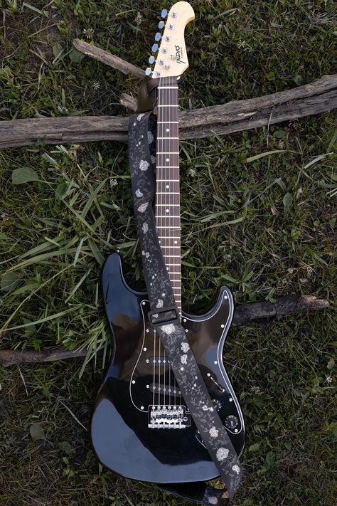 Black vine guitar strap. Printed with vines and white flowers on black background. Attached to black electric guitar laying on grass and logs Aesthetic Electric Guitar, National Park Patches, Mountain Tree, Black Electric Guitar, Electric Guitar Design, Guitar Obsession, Unique Guitars, Guitar Straps, Cool Electric Guitars