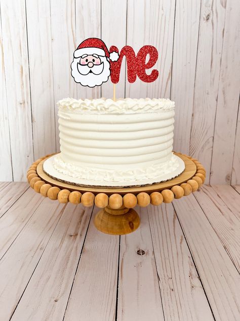 Decorate your little ones first birthday with this adorable Santa Claus cake topper. Perfect for a Christmas themed first birthday party.  CAKE TOPPER DETAILS: The cake topper measures around 6 inches wide and 3 inches tall. The cake topper is pictured on an 8 inch cake. The cake topper is made of layered cardstock and glued to a wood cake stick. CUSTOM ORDERS: Need different colors? I am able to make this cake topper in any color combination you would like. I can also change the wording displayed on the cake topper. Please contact me before purchasing, so I can make sure the custom design is possible. *Returns and exchanges will not be accepted. If you have any problems with your order, please feel free to contact me. **Click here for more Santa Claus party decor: https://www.etsy.com/sho Santa Smash Cake, Santa Claus Birthday Party, Cake Smash Christmas Theme, First Birthday Cake Christmas, Oh What Fun It Is To Be One Birthday Cake, One Year Old Christmas Birthday Party, Christmas First Birthday Cake, Christmas Smash Cake 1st Birthdays, Christmas Birthday Party Food