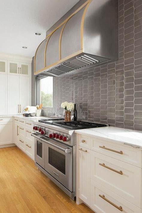 A silver and gold barrel range hood is fixed to dark gray oval backsplash tiles above a Wolf dual range flanked by white shaker cabinets finished with brass pulls. Dark Lower Cabinets, Black Lower Cabinets, Kitchen Hood Ideas, White Upper Cabinets, Two Tone Kitchen Cabinets, Lower Cabinets, Two Tone Kitchen, Oak Kitchen Cabinets, Kitchen Hoods