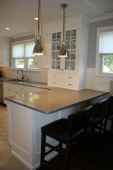 Beautiful kitchen design with Restoration Hardware Benson Pendants over peninsula bar area with black leather bar stools. White shaker cabinets with gray countertops and beveled subway tile backsplash. Glass-front built-in cabinet is used to store china and fine silverware. Kitchen with recessed lighting over polished stone floors and white roman shades covering windows. Kitchen Peninsula With Seating, Peninsula Kitchen Design, Kitchen Peninsula, Tiled Floor, Grey Countertops, Cabinets White, Beautiful Kitchen Designs, Shaker Cabinets, White Cabinetry