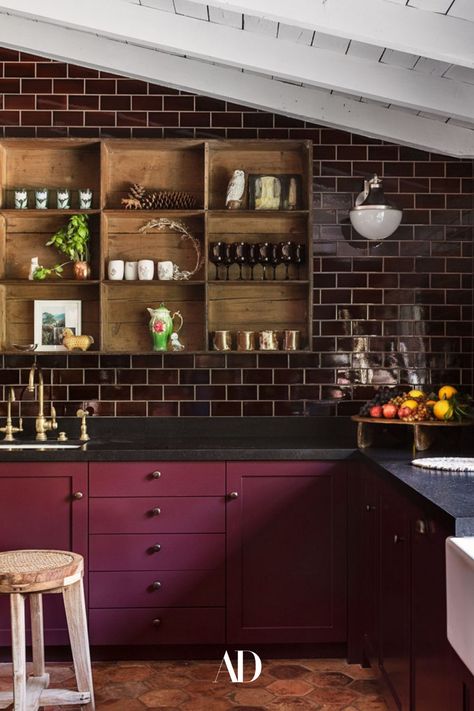 The actor and her designer opted for a darker, moodier kitchen rather than an all-white space. Aubergine wall tile by Waterworks, 19th-century terra-cotta floor tiles by Chateau Domingue, majolica backsplash and marble by Compas Stone, a cubby shelf from Nickey Kehoe, and a Pierre Jeanneret stool from Galerie Half all fill the cozy cooking space. #beams #subwaytiles #barstools #barstool #countertop #sink #beams #openshelving #cozy #kitchen #cooking #ranchhouse #ranchhome #faucet #vases #lighting Kirsten Dunst Kitchen, Kirsten Dunst Home, Dark Purple Cabinets, Kirsten Dunst House, Moody Kitchen Decor, Moody Kitchen Ideas, Moody Kitchen Design, Moody Spaces, Moody Room