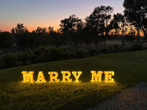 Light up “marry me” letters on a lawn overlooking hills and trees in the evening Outdoor Fall Proposal Ideas, Marry Me Signs Proposal, Marry Me Letters, Fall Proposal Ideas, Marry Me Sign, Outdoor Proposal, Engagement Decor, Light Up Letters, Light Up Signs