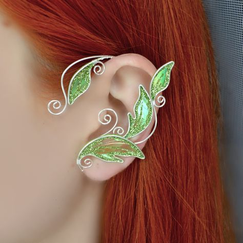 Magical elven ear cuff crafted in silver plated wire and angelina film. The film is very iridescent, so the color may vary depending on viewing angle and lightning.This elf ear cuff is available in 3 colors: emerald green, lightgreen and golden autumn. You will receive an ear cuff of your chosen colour.The ear cuff is very easy to wear. It is designed to hook over the back of your ear like a Blue Tooth device and can be gently shaped to perfectly fit your ear. No piercing needed.It is very light Ear Cuffs No Piercing, Dragon Ear Cuffs, Leaf Ear Cuffs, Elf Ear, Elf Ear Cuff, Fairy Ears, Ear Cuff Jewelry, Smiley Piercing, Cuff Earring