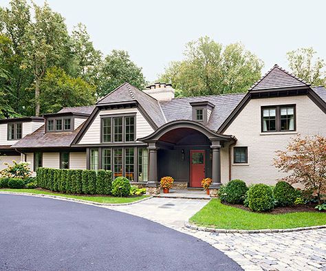 A renovation inspired by English country house design graced this exterior with abundant charm. The addition of dormers and gables, chocolate-brown trim, a cedar-shingle roof, and painted brick distinguish the home with cottagelike character; even the granite cobbles edging the path to the columned front entry evoke storybook appeal. Ranch House Remodel, Best Exterior Paint, Dark Trim, Brown Roof, Country House Design, Exterior Color Schemes, Exterior Paint Colors For House, House Siding, Ranch Style Homes