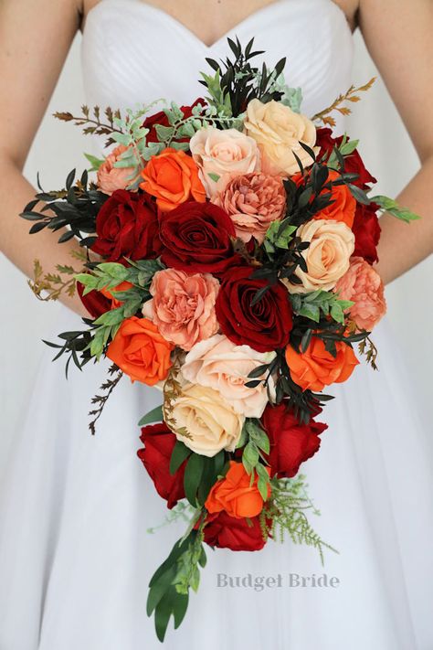 This lovely assortment of red, orange, champagne and sand colored roses is bound to turn heads on your wedding day. This lovely cascading brides’ bouquet from the is an absolutely breathtaking arrangement for any bride to be, in any season. Bright greenery and dusty peach peony accents complete the look and add a delicate realism to this beautiful bouquet. This bouquet is 10” wide, 18” long, and is crafted by our in-house florists without using a foam base to anchor the flowers to the bouquet. I Mexican Style Wedding Bouquet, Mexican Bouquet Wedding, Mexican Wedding Flowers Bridal Bouquets, Red And Orange Wedding Decorations, Orange Rose Bouquet Wedding, Orange And Red Wedding Flowers, Fall Color Bouquet, Red Orange Pink Wedding Color Palettes, Red And Orange Bouquet