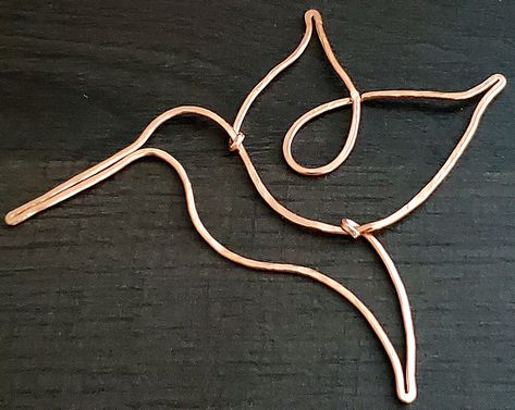 A hummingbird is shaped out of copper wire, resting on a dark colored wood grain desk. Wire Hummingbird Suncatcher, Copper Wire Diy Crafts, Cooper Wire Art, Wire Hummingbird Diy, Copper Wire Art Diy, Wire Hummingbird, Wire Shaping, Wire Dragonfly, Wire Shapes