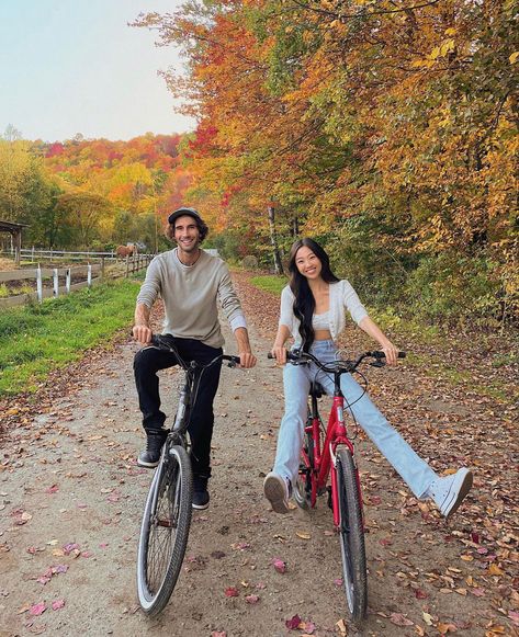 A couple is smiling at the camera as they are riding bikes past trees with orange and yellow leaves. They are enjoying the perfect fall date idea. Couples Riding Bikes, Active Couple Aesthetic, Biking Date, October Date Ideas, Bike Ride Date, Couple Bike Ride, Date Movie Night, Cute Fall Date Ideas, Active Date Ideas