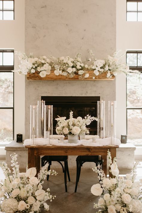 Dramatic white blooms and tall taper candles frame a bridal bouquet on a farmhouse sweetheart table making the perfect table for two. Bridal Bouquet Sweetheart Table, Sweetheart Table Bridal Bouquet, Bridesmaids Bouquets On Sweetheart Table, Sweetheart Table Fireplace, Fireplace Sweetheart Table, Sweetheart Table Wedding Fireplace, Sweet Heart Table Wedding Romantic, Lovers Table Wedding, Sweetheart Table Candles On Floor