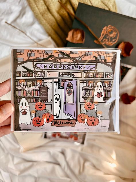 Have A Bookish 👻 Halloween Greeting Card  This illustrated greeting card features a haunted bookstore scene with a hand holding the door open, inviting the recipient inside. This card is perfect for anyone who loves books and Halloween. The spooky bookstore scene is sure to delight anyone who enjoys a good scare. Cards Details:  * Folded With Blank Interior  * 4.25 x 5.5 inches in size * Thick White Cover Stock * Matching with a white envelope that has a self-seal strip for saving time.  * High-quality paper 👻 Perfect for Bookish and Bookclub Halloween Party  👻 This greeting card is perfect for anyone who loves Halloween. 👻 Great for Book Lovers This greeting card is also perfect for book lovers. The Halloween bookstore vibe surely brings joy and a smile to every book lover of any age. Haunted Bookstore, Halloween Journaling, Bookish Halloween, Fall Gift Baskets, Halloween Gift Baskets, Greeting Card Birthday, Halloween Greeting Card, Book Room, Pumpkin Candy