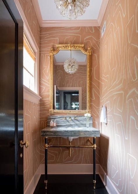 Lined with salmon pink crown moldings and baseboards, walls clad Kelly Wearstler Groundworks Graffito Wallpaper accent a contemporary pink and black powder room boasting a gold French mirror hung over a gray stripe marble sink vanity. Kelly Wearstler Powder Room, Graffito Wallpaper, Grey Powder Room, Black Powder Room, Wallpaper Powder Room, Hexagon Floor, Floating Sink, Powder Room Wallpaper, Marble Sink