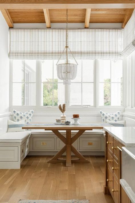 Hung from a brown wood plank ceiling over a square trestle dining table, a white beaded chandelier lights a breakfast nook finished with a built-in u-shaped dining bench. White Beaded Chandelier, Latest Kate, Designers Portfolio, Neutral Interior Design, Wood Plank Ceiling, Kate Marker Interiors, Plank Ceiling, Transitional Dining Room, Transitional Dining