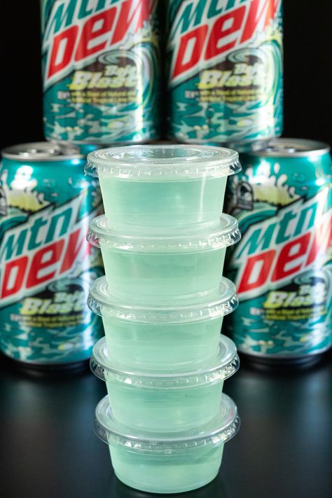 A stack of light blue Baja blast jello shots in front of cans of the soda. Margarita Jello Shots Tequila, Best Margarita Jello Shots, Vodka Jello Shots Easy, Margarita Jell-o Shots, Baja Blast Alcohol Drink Recipes, Baja Blast Margarita, Camping Jello Shots, Mountain Dew Mixed Drinks, Tajin Jello Shots