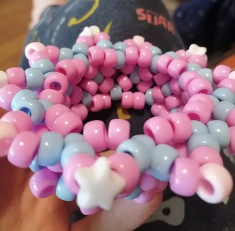 a baby pink and pastel blue x-base cuff. on the side nearest to us, there are blue-pink-white protruding triangles, half of them ending with stars. the background is a pajama pant and the distant floor Pastel Kandi, Pastel Clown, Candy Cotton, Emu Otori, Kandi Cuff, Emu, Perler Beads, Cute Jewelry, Pastel