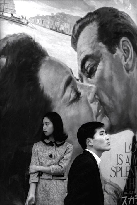 Henri Cartier-Bresson photo of a man and woman standing juxtaposed against a painted background of a couple kissing. Photography juxtaposition examples. Robert Frank, Robert Doisneau, Henri Cartier Bresson, French Photographers, Famous Photographers, Great Photographers, Magnum Photos, Foto Art, Candid Photography