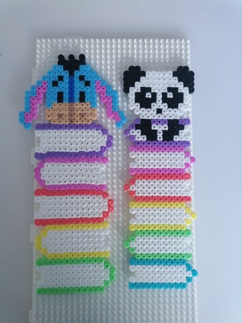 Handmade bookmarks from perler beads. Left one is a stack of books with eeyeore on top. Right one is a stack of books with a panda on top Perler Bead Book Pattern, Pyssla Ideas Bookmark, Hama Beads Bookmark Ideas, Hama Beads Bookmarks, Perler Art Ideas, Cute Perler Bead Bookmarks, Disney Perler Beads Ideas, Book Perler Bead Patterns, Iron Beads Bookmark