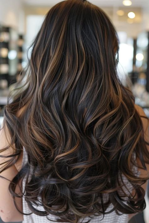 Long, wavy hair with dark brown and caramel highlights, styled in loose curls in a salon setting. Winter Highlights For Black Hair, Black And Caramel Balayage, Highlight In Black Hair, Black Wavy Hair With Highlights, Partial Highlights On Black Hair, Caramel Partial Highlights, Black Hair With Lowlights Balayage, Trendy Highlights For Black Hair, Black Hair With Golden Highlights